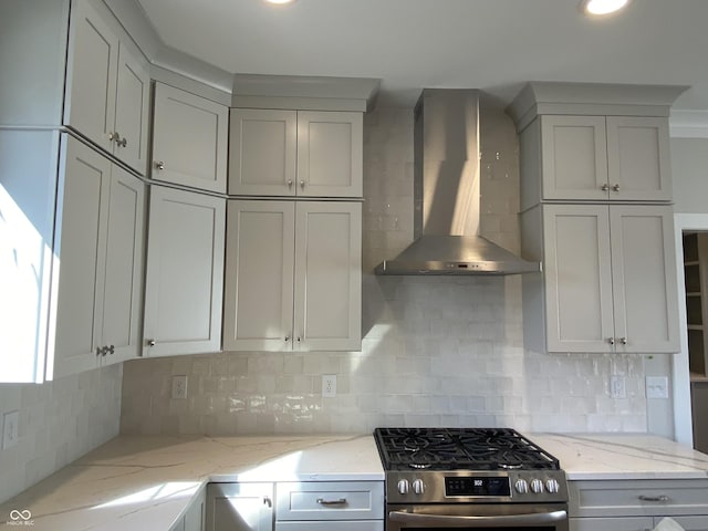 kitchen featuring gray cabinetry, stainless steel gas range, backsplash, light stone countertops, and wall chimney exhaust hood