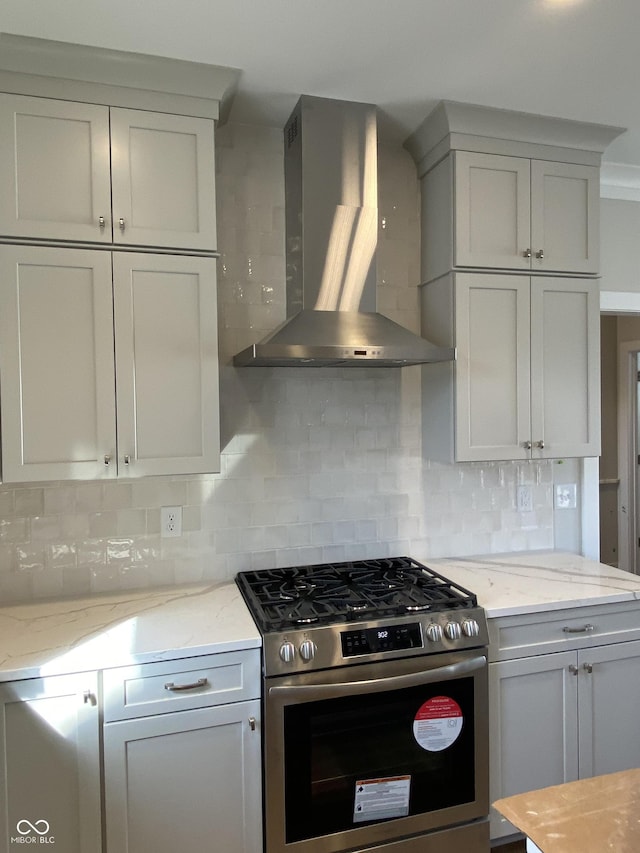 kitchen featuring stainless steel gas range oven, light stone counters, wall chimney range hood, white cabinetry, and backsplash