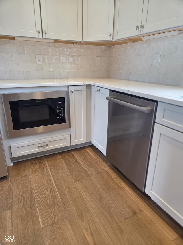 kitchen with decorative backsplash, dark wood-style flooring, white cabinetry, built in microwave, and stainless steel dishwasher