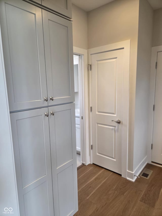 corridor featuring dark wood-type flooring, baseboards, and visible vents