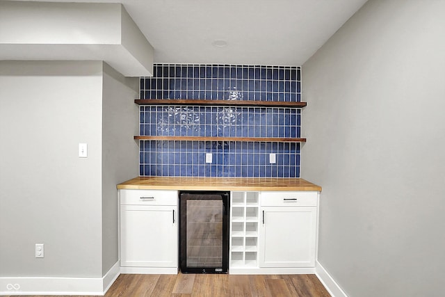 bar featuring baseboards, wood finished floors, tasteful backsplash, and beverage cooler