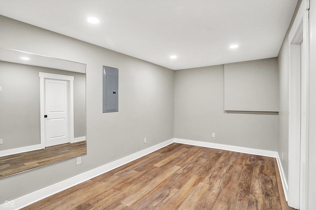 unfurnished room featuring electric panel, baseboards, wood finished floors, and recessed lighting