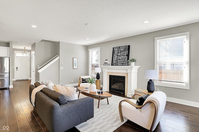 living room with dark wood finished floors, a glass covered fireplace, stairs, and baseboards