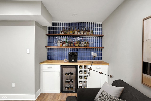 bar with beverage cooler, backsplash, light wood-style floors, baseboards, and a dry bar