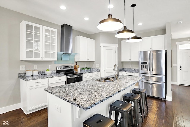 kitchen featuring glass insert cabinets, wall chimney range hood, a kitchen bar, stainless steel appliances, and a sink