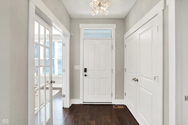 foyer entrance with dark wood finished floors, an inviting chandelier, visible vents, and baseboards