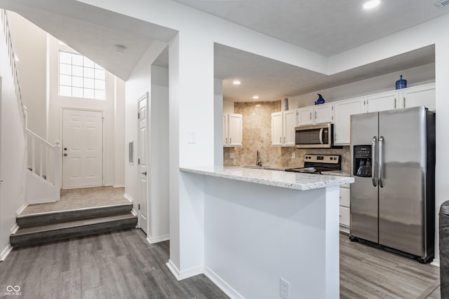 kitchen featuring dark wood-type flooring, white cabinets, appliances with stainless steel finishes, decorative backsplash, and light stone countertops