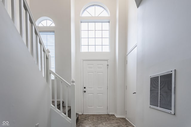 entryway with stairway, visible vents, a healthy amount of sunlight, and a towering ceiling