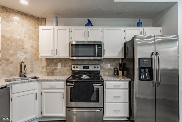 kitchen with backsplash, appliances with stainless steel finishes, white cabinetry, a sink, and light stone countertops