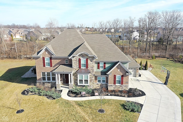 view of front facade with stone siding, a shingled roof, a front yard, and driveway