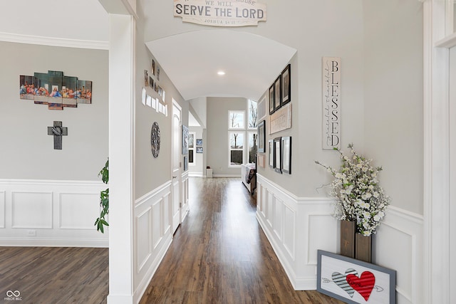 corridor featuring crown molding, dark wood-type flooring, wainscoting, and a decorative wall