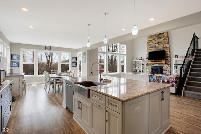 kitchen with dark wood-style floors, light stone counters, a center island with sink, a sink, and dishwasher