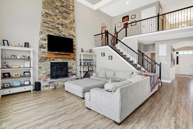 living room with arched walkways, a fireplace, stairway, a towering ceiling, and wood finished floors