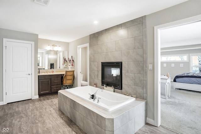 ensuite bathroom featuring visible vents, baseboards, vanity, a fireplace, and a bath