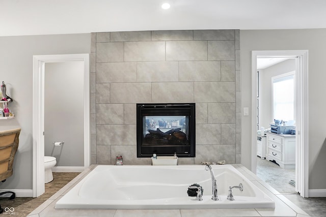 bathroom with toilet, baseboards, a bath, and a multi sided fireplace