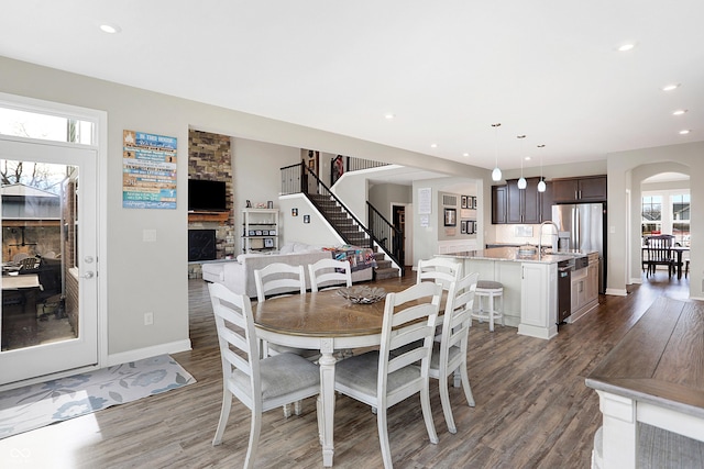 dining area featuring arched walkways, a stone fireplace, recessed lighting, wood finished floors, and stairs