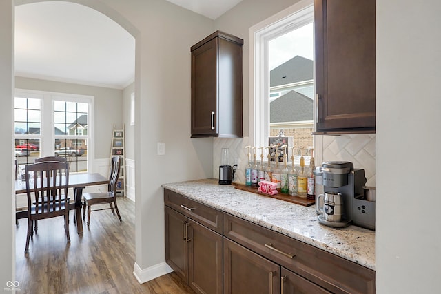 bar featuring a dry bar, light wood finished floors, tasteful backsplash, and arched walkways