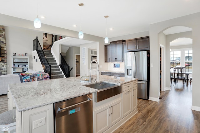 kitchen featuring appliances with stainless steel finishes, open floor plan, wood finished floors, a kitchen island with sink, and a sink