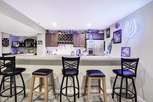 bar featuring recessed lighting, baseboards, stainless steel fridge with ice dispenser, decorative backsplash, and wet bar