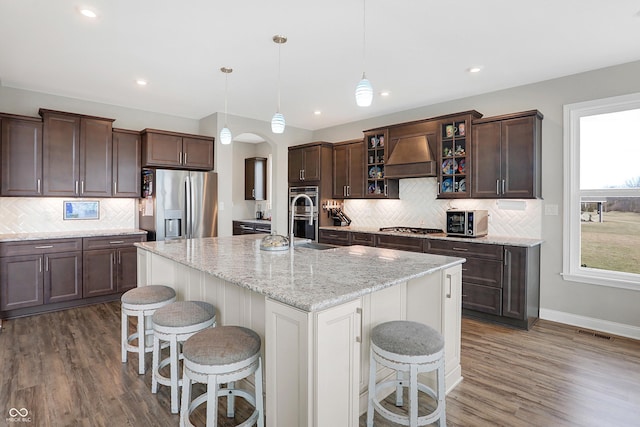 kitchen with arched walkways, a breakfast bar area, stainless steel appliances, premium range hood, and visible vents