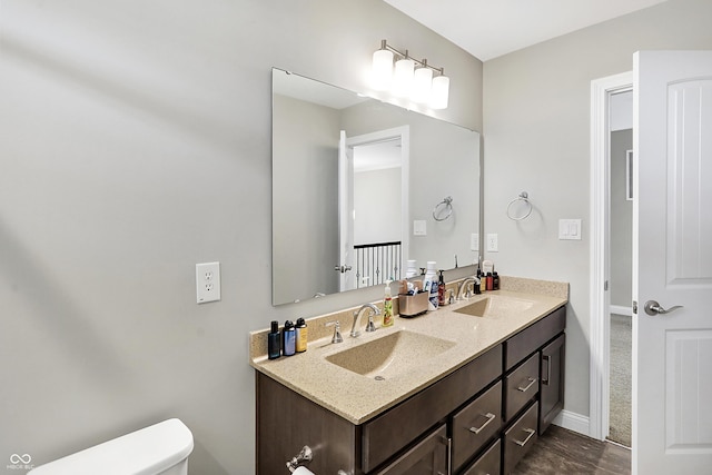 bathroom featuring toilet, double vanity, baseboards, and a sink