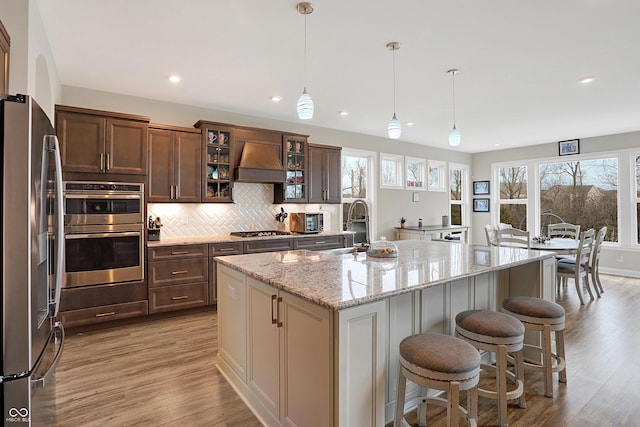 kitchen featuring decorative backsplash, appliances with stainless steel finishes, custom exhaust hood, light wood-type flooring, and a sink