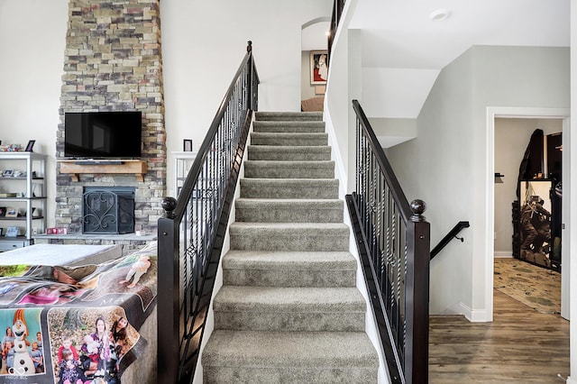 staircase with a stone fireplace, wood finished floors, and baseboards