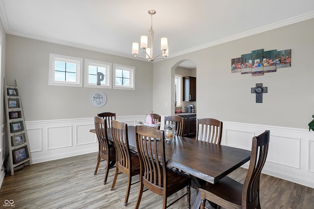 dining area with arched walkways, a wainscoted wall, ornamental molding, wood finished floors, and a notable chandelier