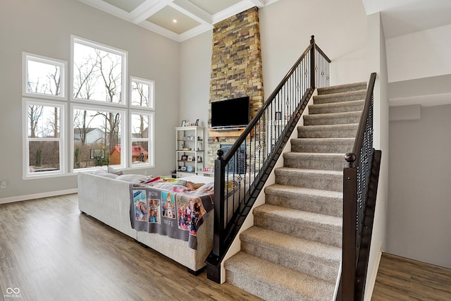 stairs with beam ceiling, a high ceiling, wood finished floors, coffered ceiling, and baseboards