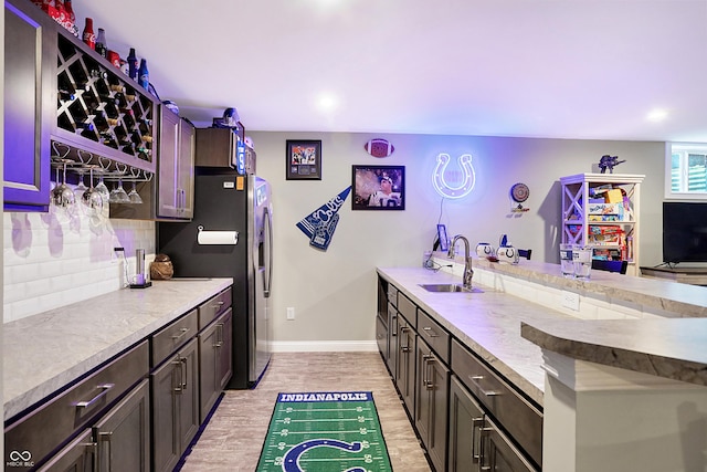 kitchen featuring tasteful backsplash, light wood-style flooring, a peninsula, stainless steel refrigerator with ice dispenser, and a sink