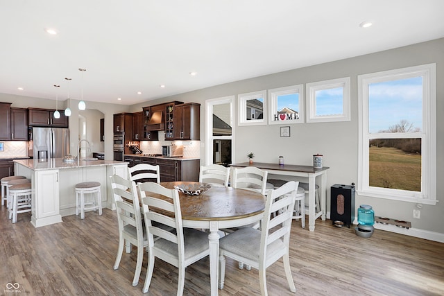 dining area with arched walkways, baseboards, light wood finished floors, and recessed lighting