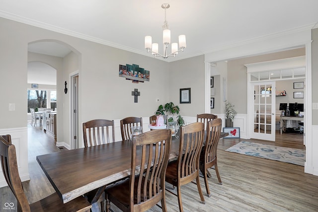 dining space with arched walkways, crown molding, light wood-style flooring, an inviting chandelier, and wainscoting