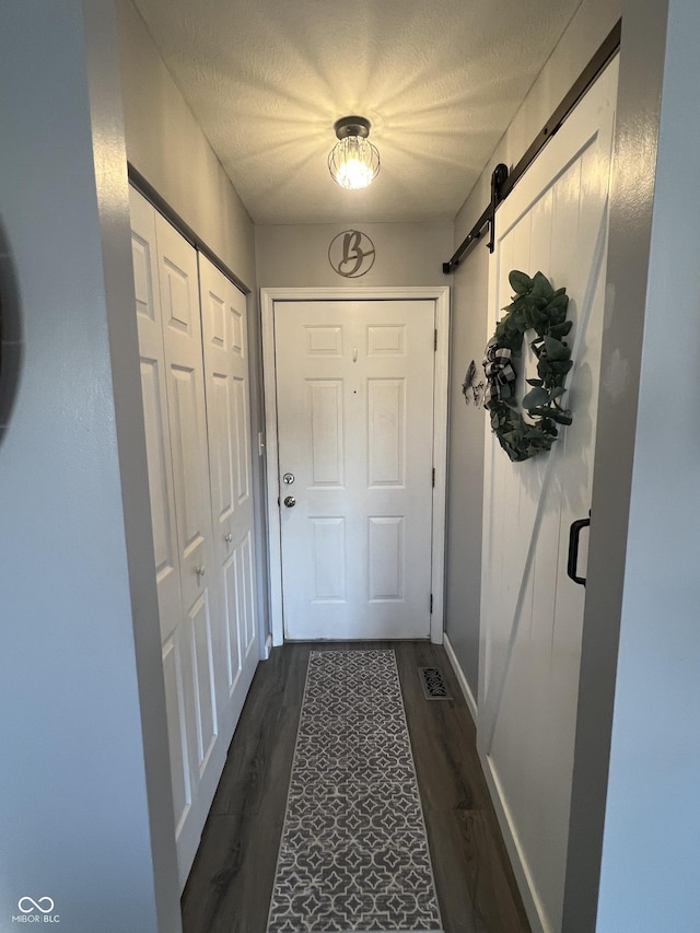 doorway featuring a barn door, a textured ceiling, visible vents, and dark wood-style flooring