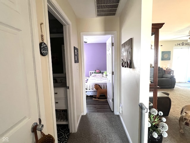 hall featuring baseboards, visible vents, dark colored carpet, and a sink