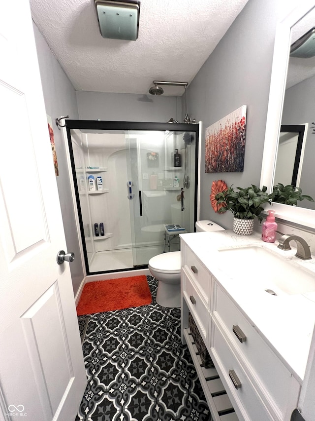 full bath with vanity, a textured ceiling, a shower stall, and toilet