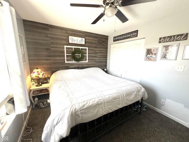 bedroom featuring an accent wall, baseboards, ceiling fan, wood walls, and carpet flooring