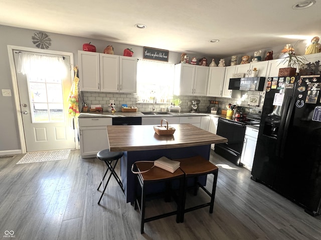 kitchen featuring dark wood-type flooring, butcher block countertops, decorative backsplash, black appliances, and a sink