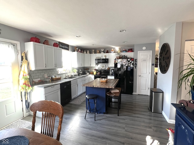 kitchen with tasteful backsplash, dark wood finished floors, butcher block counters, black appliances, and a sink