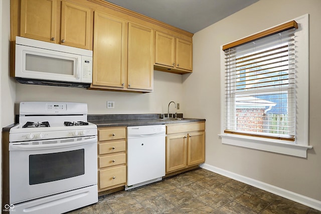 kitchen featuring dark countertops, light brown cabinetry, a sink, white appliances, and baseboards