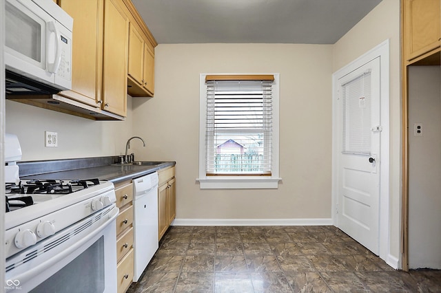 kitchen with white appliances, baseboards, dark countertops, light brown cabinets, and a sink