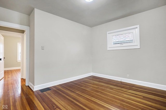 spare room featuring dark wood-type flooring, visible vents, and baseboards