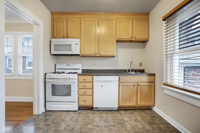 kitchen with white appliances, baseboards, dark countertops, light brown cabinetry, and a sink