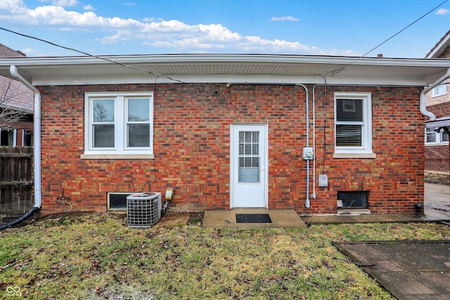 rear view of house with central AC unit, a lawn, and brick siding