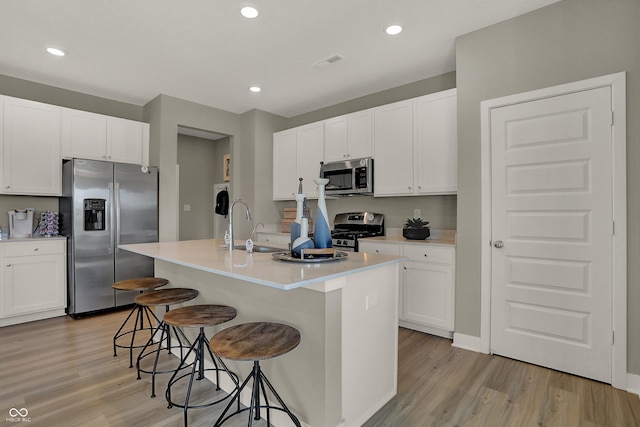 kitchen featuring a breakfast bar, light wood finished floors, stainless steel appliances, visible vents, and a sink