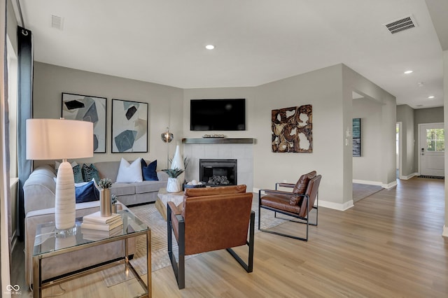 living area with recessed lighting, visible vents, a tiled fireplace, light wood-style floors, and baseboards