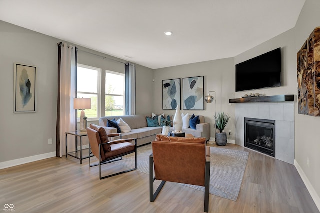 living room featuring light wood-type flooring, a tile fireplace, and baseboards