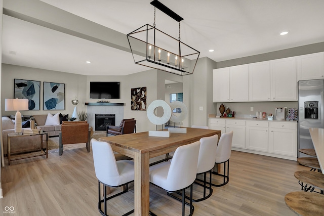 dining area with light wood-type flooring, recessed lighting, and a tile fireplace