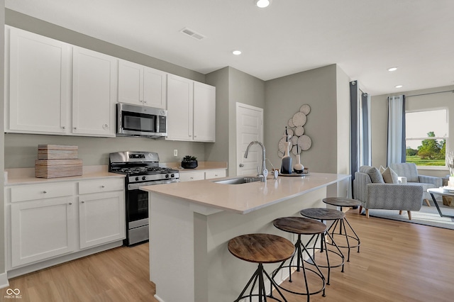 kitchen featuring light wood finished floors, visible vents, stainless steel appliances, a kitchen bar, and a sink