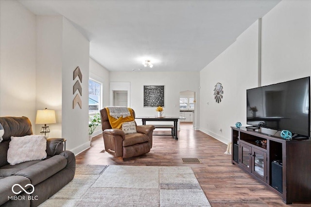 living area with arched walkways, baseboards, wood finished floors, and a healthy amount of sunlight