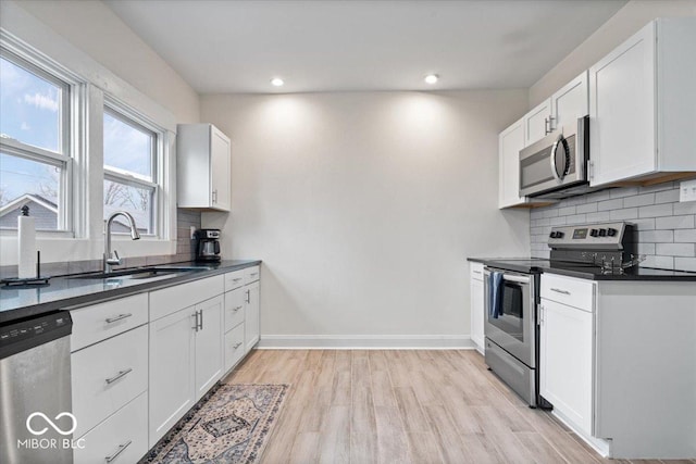 kitchen featuring a sink, baseboards, appliances with stainless steel finishes, light wood-type flooring, and dark countertops